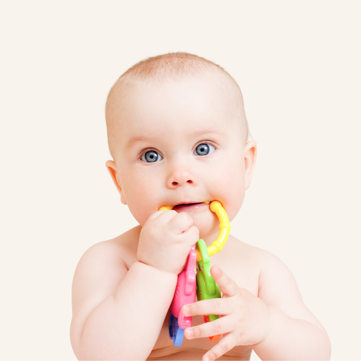 A baby with blue eyes holds and chews on colorful plastic teething rings against a plain light background.